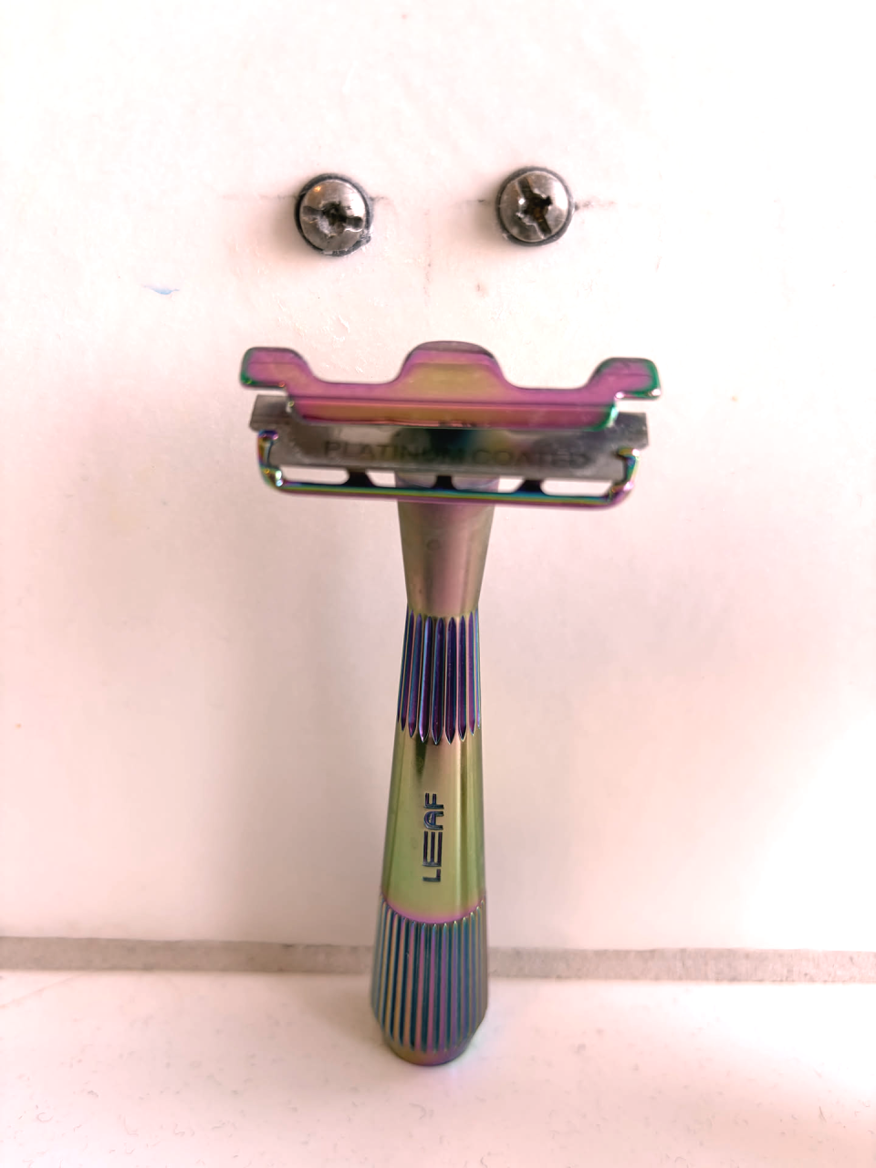 Ein Rasierer steht vor einer Wand. Knapp über ihm sind zwei Schrauben in der Wand. Zusammen ergibt das ein freundliches Gesicht.