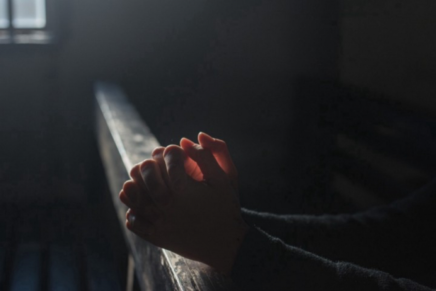 Eine Person die sitzend auf einer Kirchenbank betet. Man sieht nur die Hände der Person
