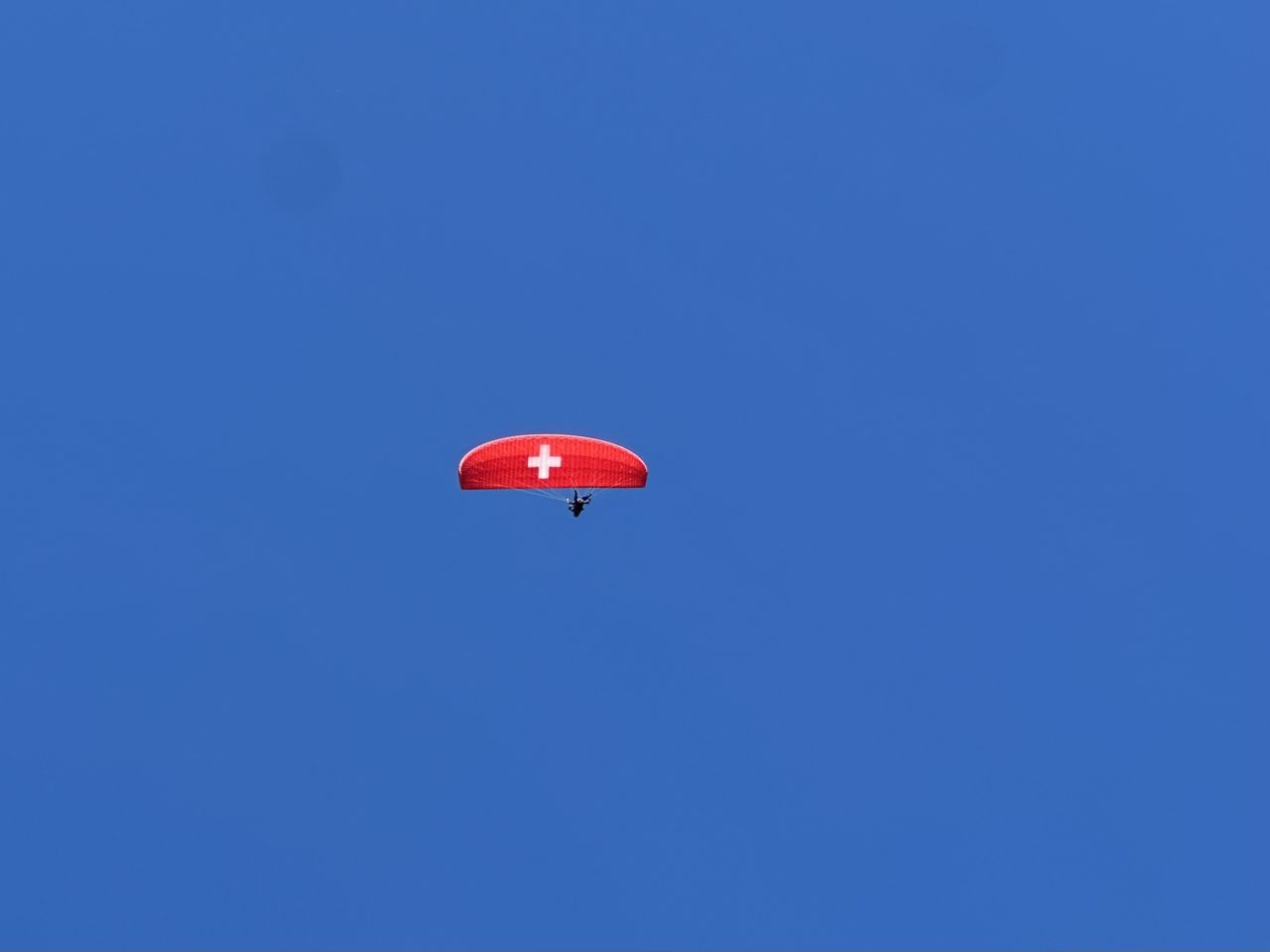 Ein roter Gleitschirm (mit weissem Kreuz) am blauen Himmel